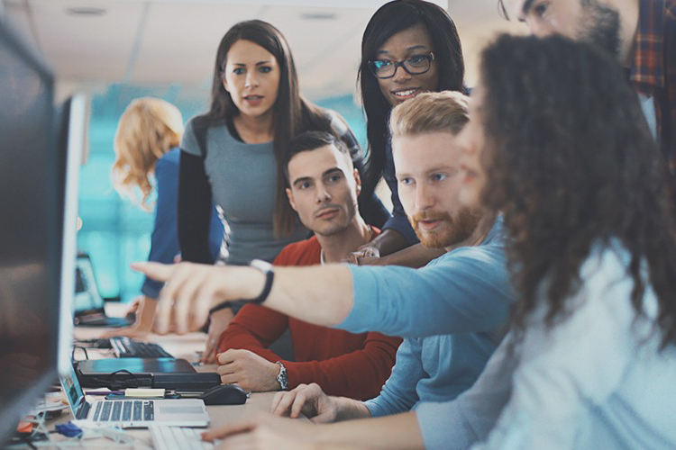 Group of people sat around a computer have a discussion